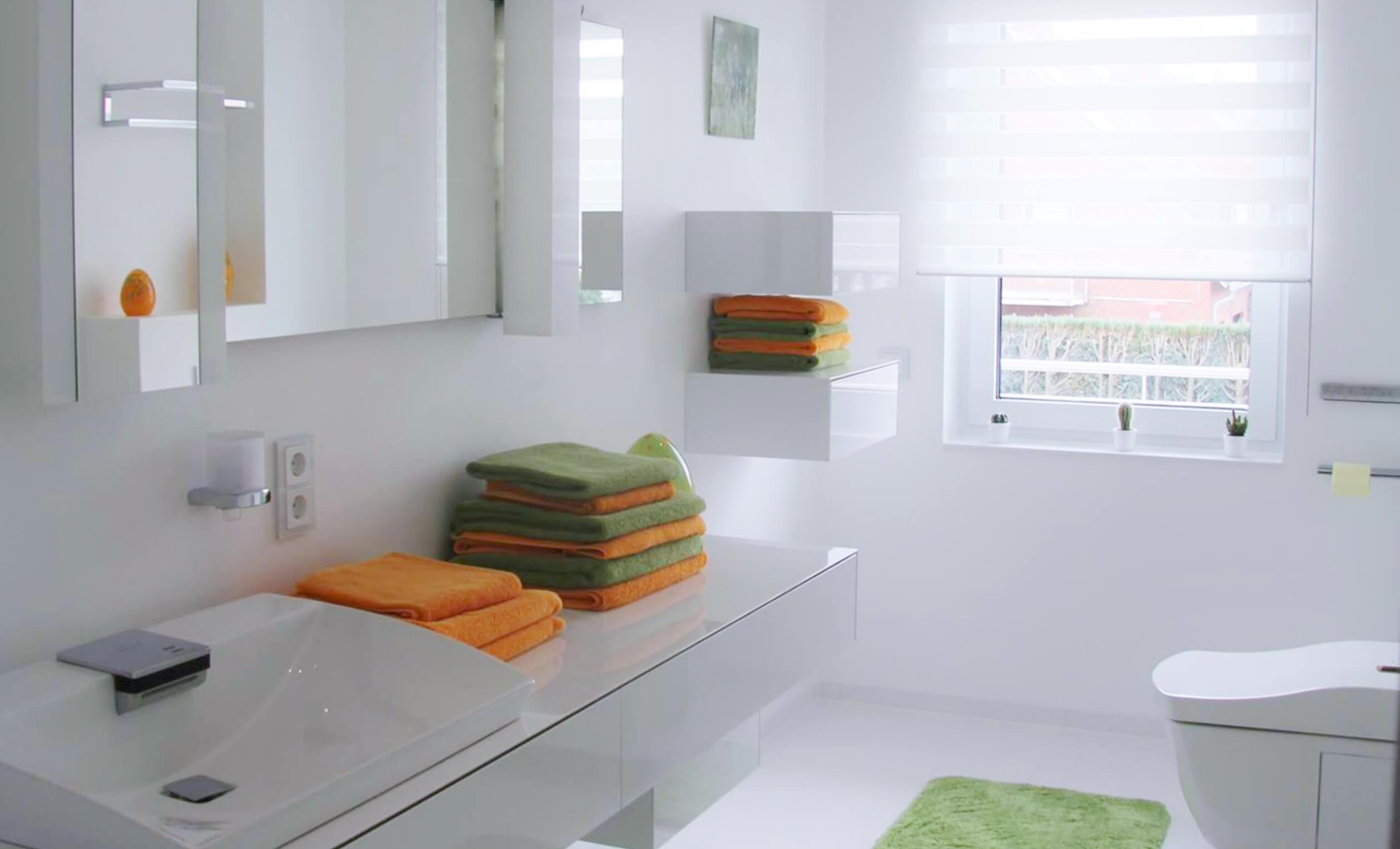 Gäste-WC in Weiß mit Washlet und modernem Waschtisch samt orange-grüner Handtuchstapel