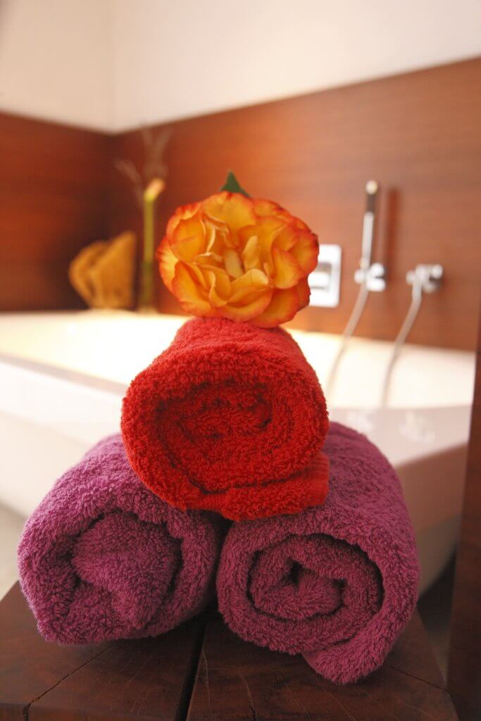 Drei zusammengerollte Handtücher mit Blume und Badewanne im Hintergrund