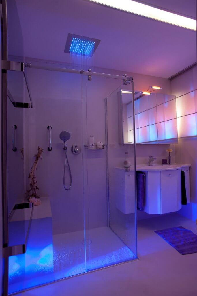 Gästebad mit Regenbrause Stimmungsvolle Lichtszenarien im Badezimmer Die Farbtherapie harmonisiert das körperliche und das seelische Wohlbefinden mit Hilfe von Farben. Diese verfügen über eine bestimmte Wellenlänge, die je nach Farbton einen entspannenden oder vitalisierenden Effekt aufweist. Die hinter einer transparenten Glaswand verborgene Regendusche mit LED Leuchten besitzt eine intuitiv zu bedienende Schaltfläche, auf der die einzelnen Impulse individuell eingestellt werden können. Auch eine Programmierung im Voraus erlaubt es in der Früh mit den Strahlen einer aufgehenden Sonne aufzustehen.