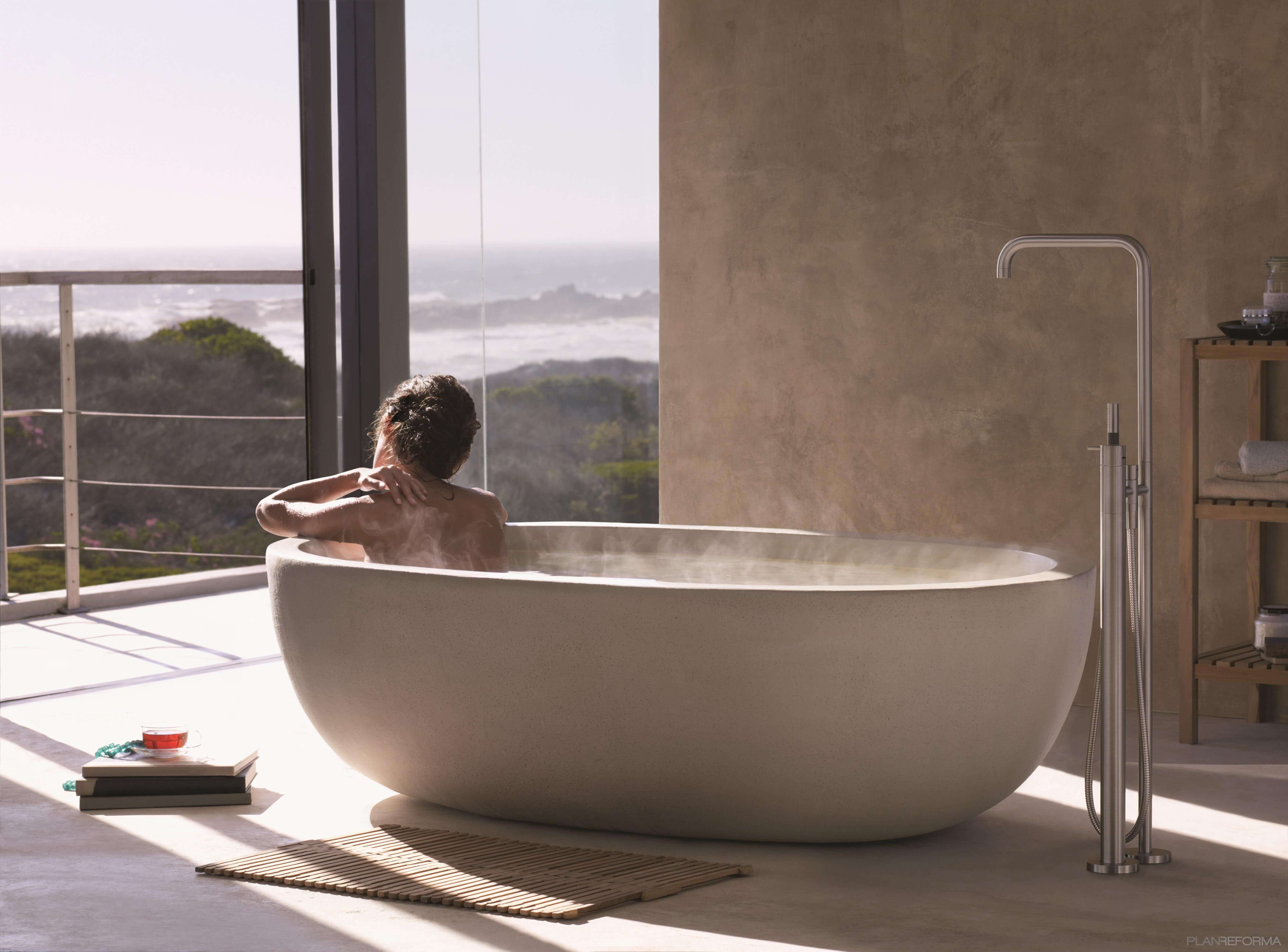 Frau in ovaler Badewanne aus Naturstein mit Naturblick nimmt Milch Honig Bad