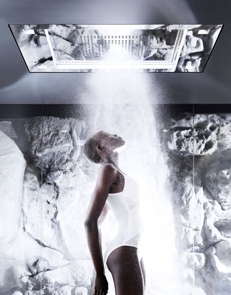 Schwarze Person in weißem Badeanzug unter der laufenden Luxusdusche von Dornbracht