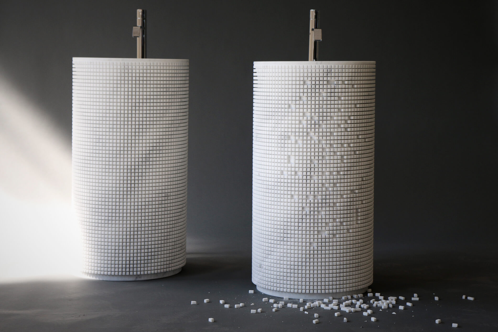 Zwei zylindrische Waschtonnen mit weißem Mosaik - eine komplett, die andere mit herausgelösten Steinchen
