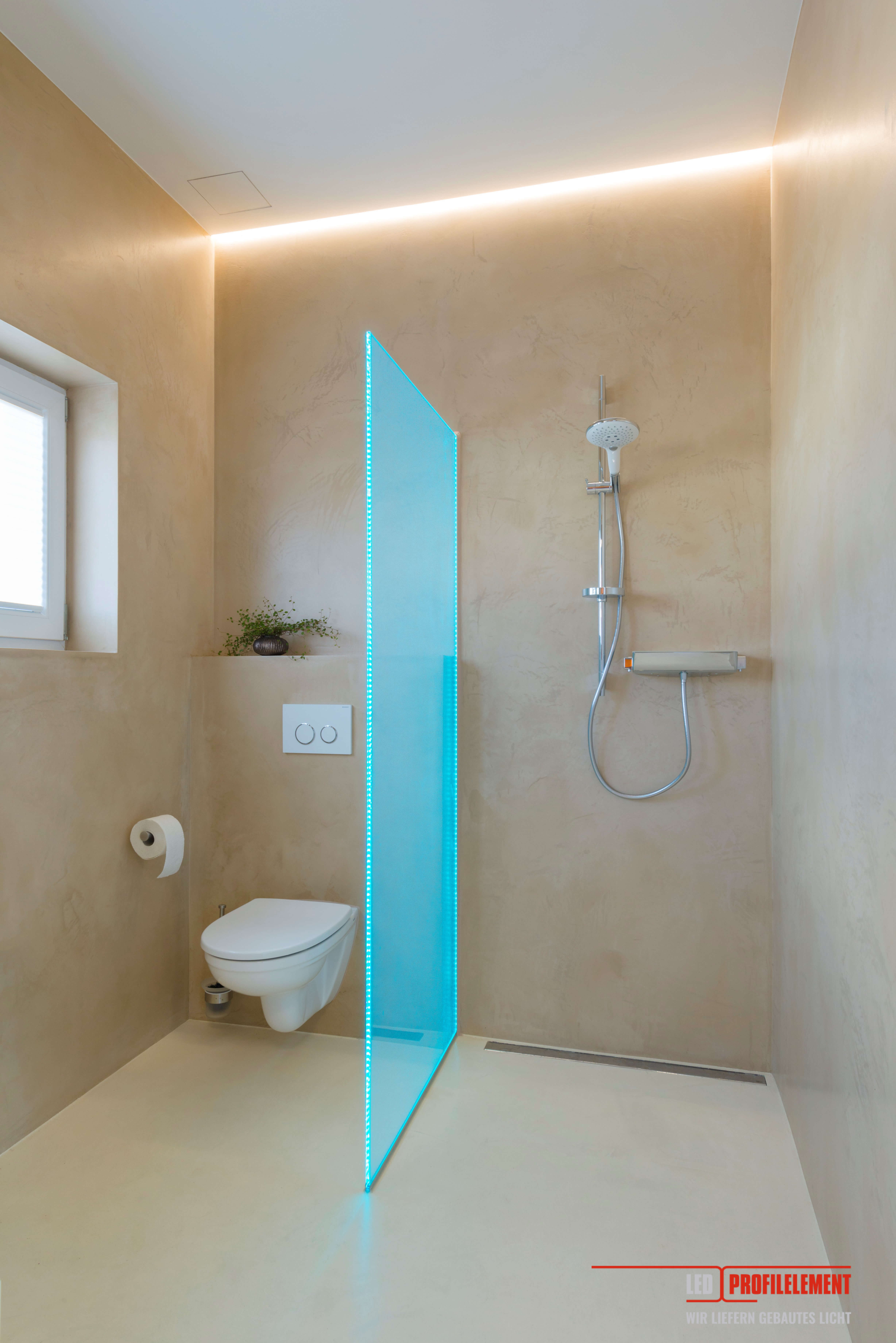 Kleines Bad mit Lichtleiste entlag der Wandkante, Toilette und mittels beleuchteter Duschwand abgetrennter Duschbereich