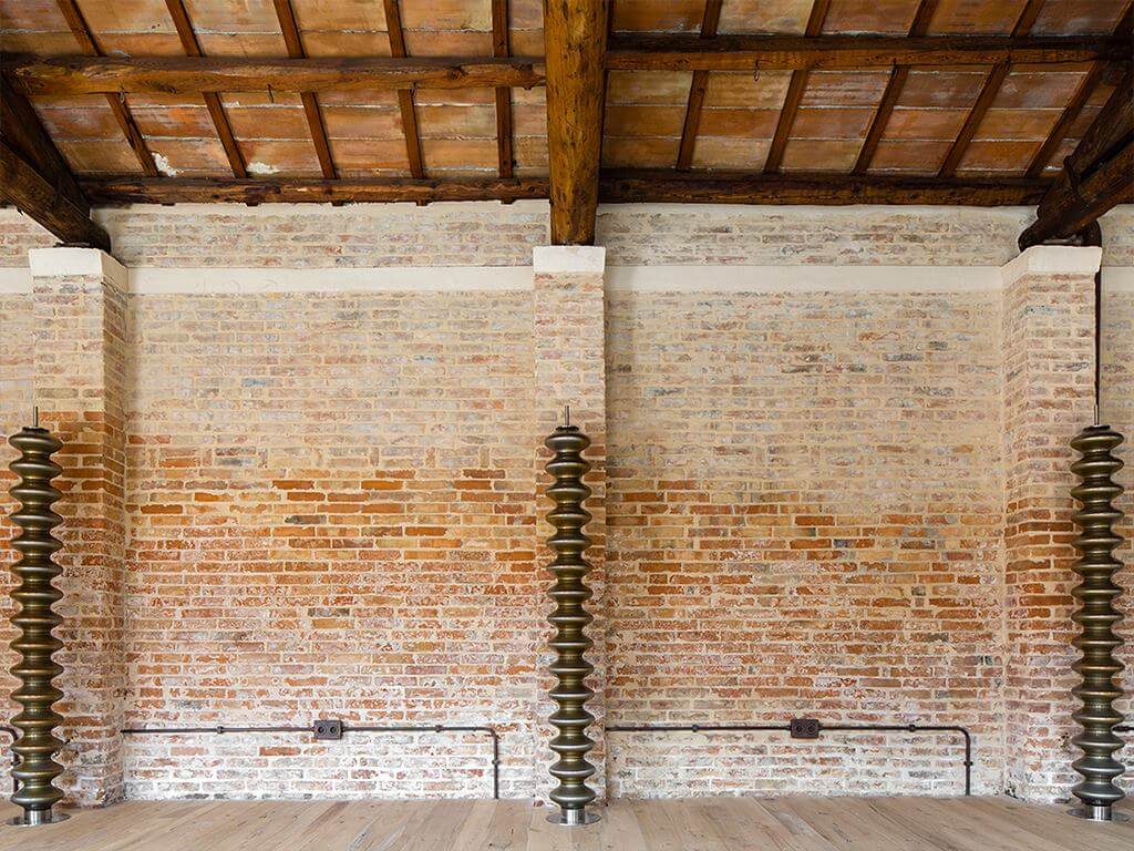 Ziegelwand mit drei Tubes Heizkörpern Ziegelwand und Holzbalken an der Decke mit drei vertilalen braunen Tubes Heizkörpern in Wellenform