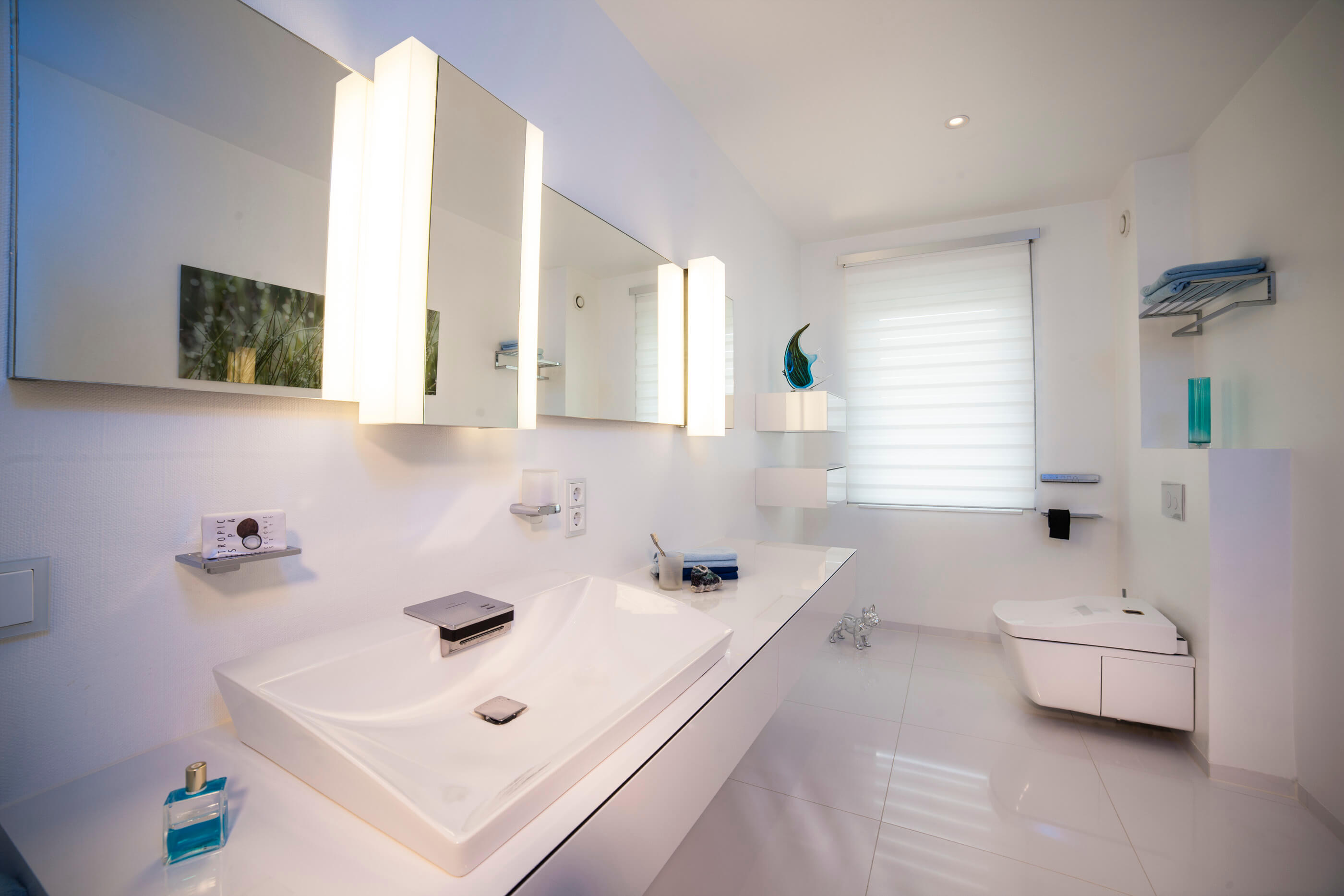 Kleines Bad in Weiß mit Washlet und Waschbereich damt großem, beleuchtetem Spiegel
