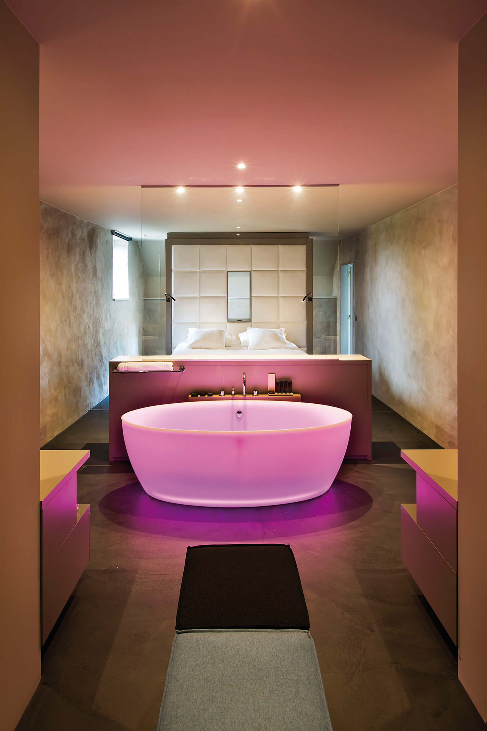 Doppelbett mit smarter Badewanne davor in violettem Licht