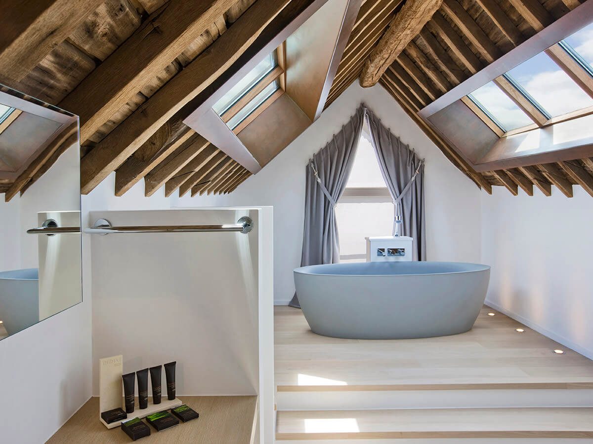 Freistehende Luxusbadewanne in Bad mit hölzernen Dachbalken und großen Fenstern