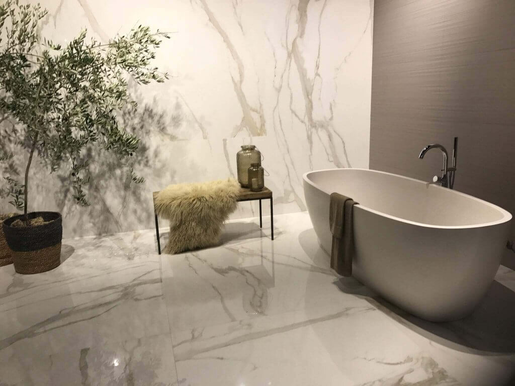Freistehende Badewanne mit Sitznbank und Accessoires zwischen marmorgefliestem Boden und Wand