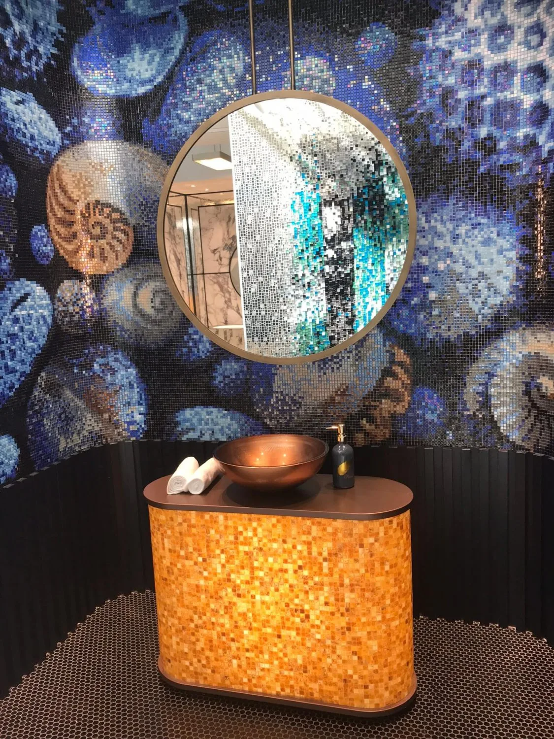 Kupferfarbenes Aufsatzwaschbecken auf Waschtisch mit bernsteinfarbenem Mosaik vor einer blauen Mosaikwand