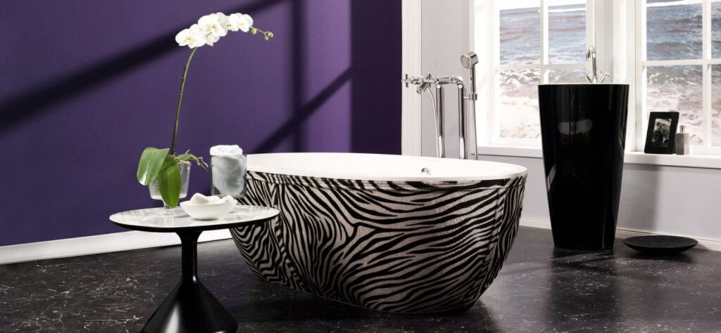Luxus Badewanne im Zebra-Muster vor violetter Wand und schwarzer zylindrischer Waschsäule