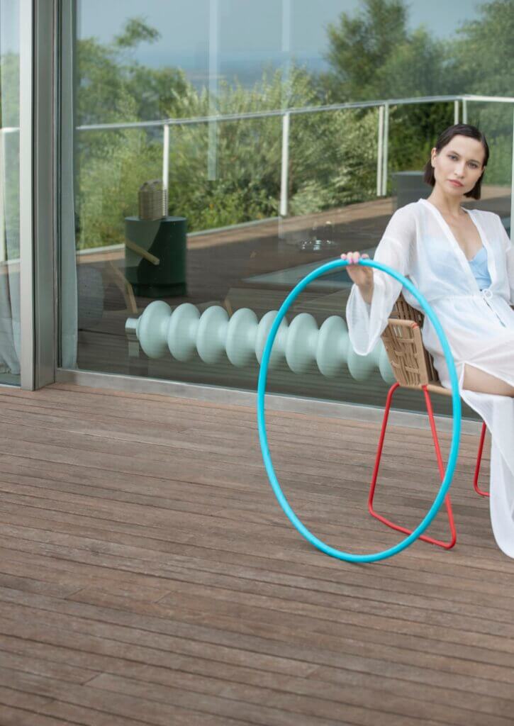 Frau mit Hulahoop-Reifen auf Terrasse - hinter der Glastüre liegt ein wellenförmiger TubnesHeizkörper in Weiß