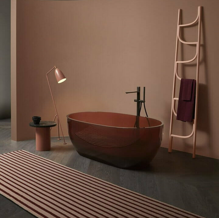 Präsentation von Antonio Lupi: Gläserne Badewanne in dunklem Rosaton mit Leiter und Teppich vor Wand in Altrosa