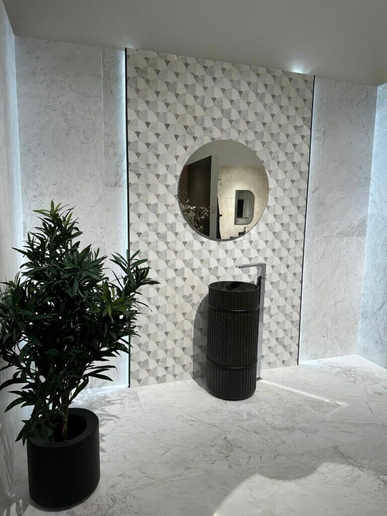 Schwarze Waschtonne mit rundem Spiegel vor geprägter Fliesenwand