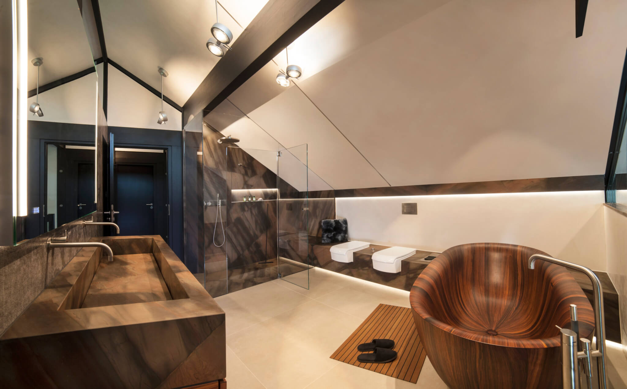 Modernes Badezimmer mit Natursteinelementen in Dusche, am Waschbecken und WC sowie einer Holzwanne