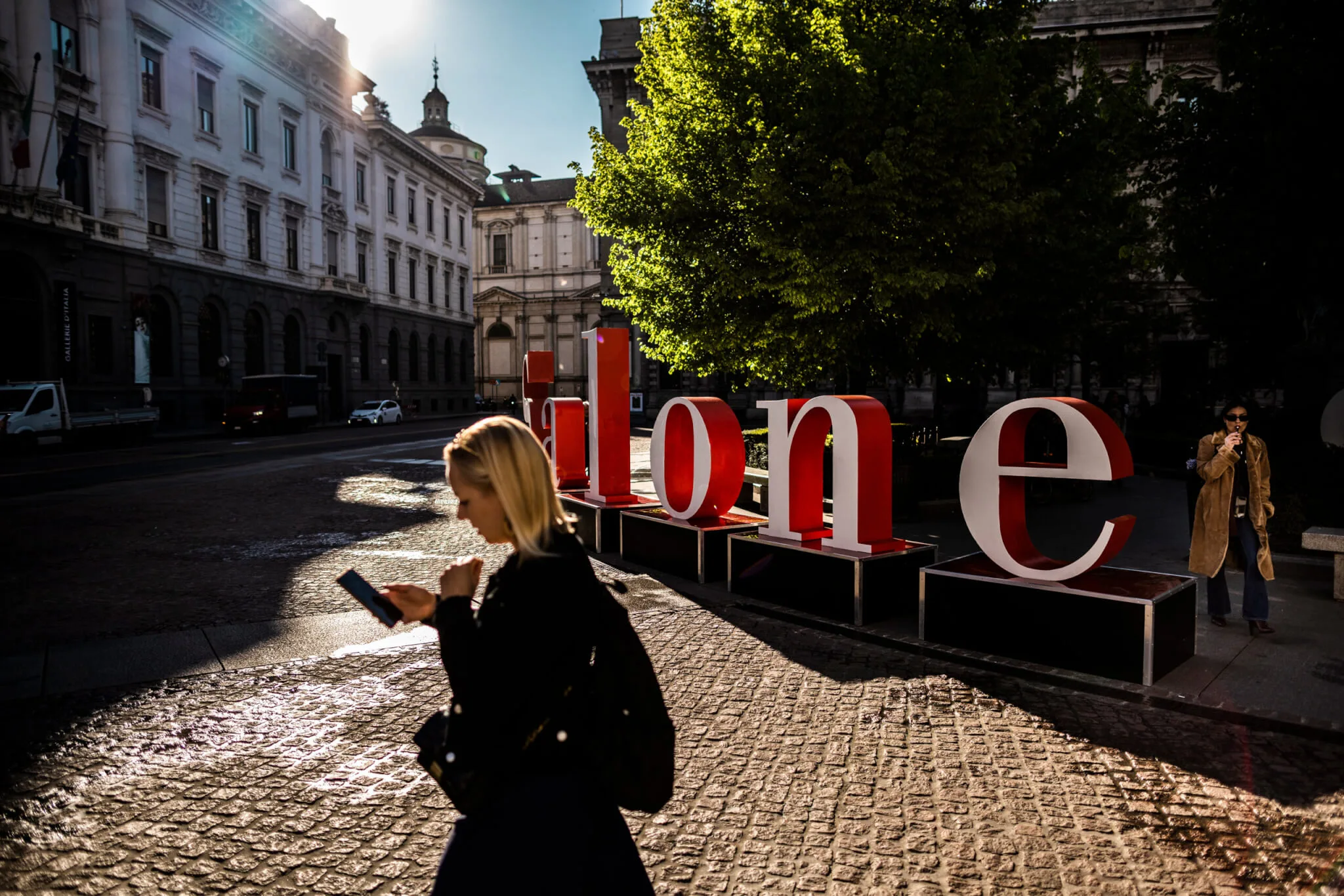 Straßenszene mit Plakaten und Anzeigen für die Messe im Hintergrund, während Passanten die Stadt erkunden.