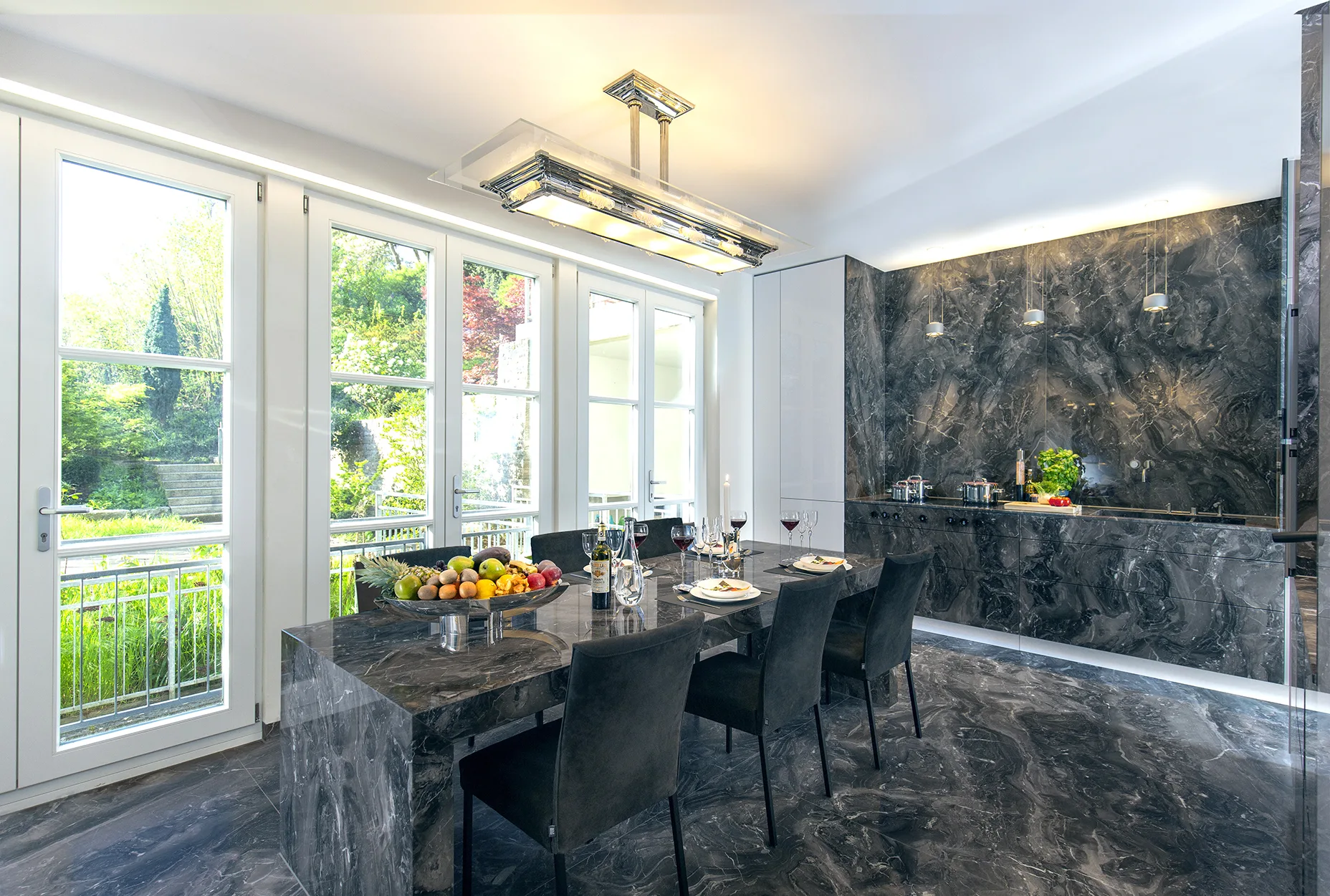Blick in den Garten über den luxuriösen Naturstein-Tisch mit Einblick in die Küchenzeile