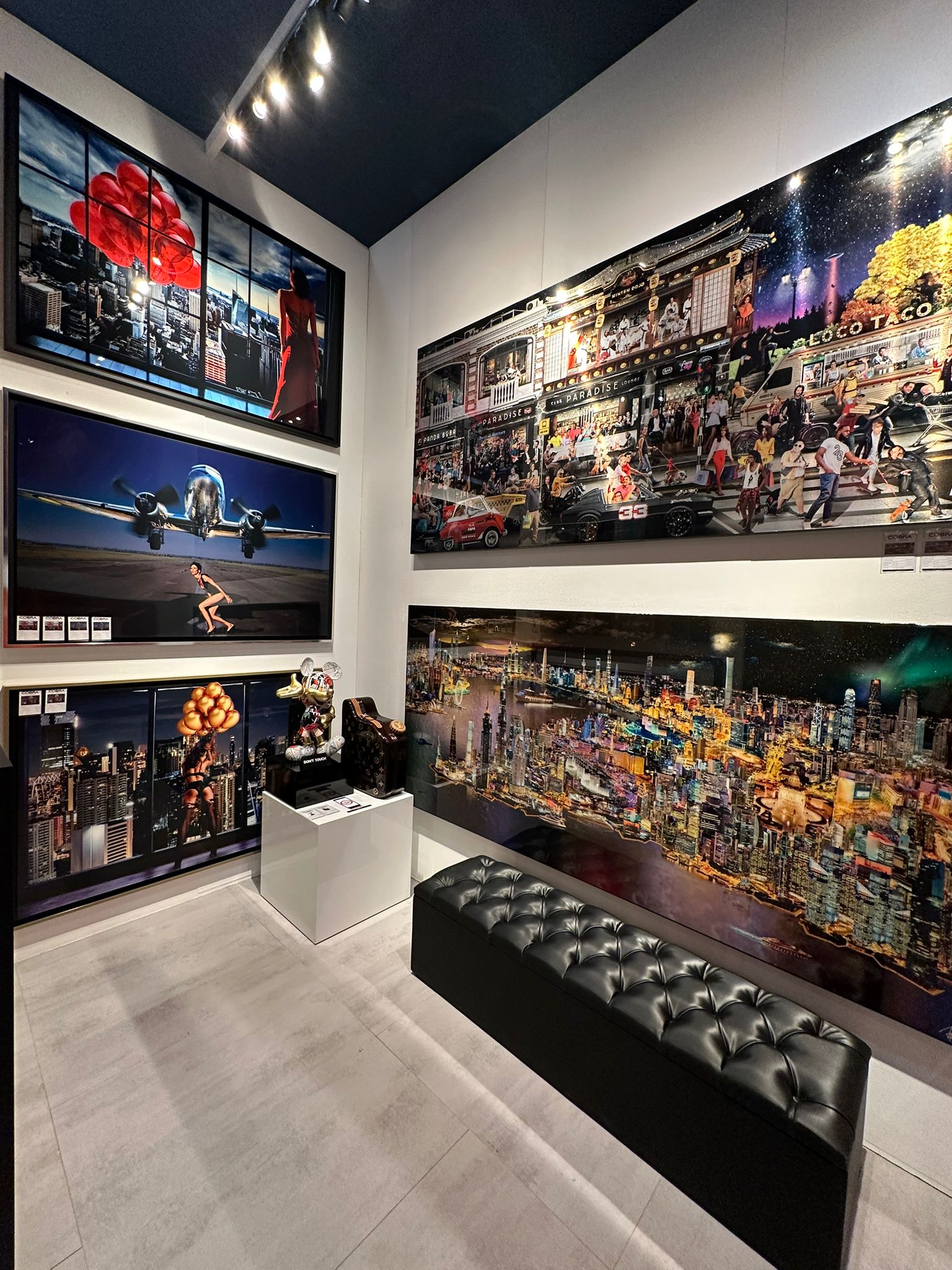 Moderne Kunstwerke mit urbanen und futuristischen Themen, präsentiert in einer Galerie mit elegantem Interieur und schwarzer Polsterbank.