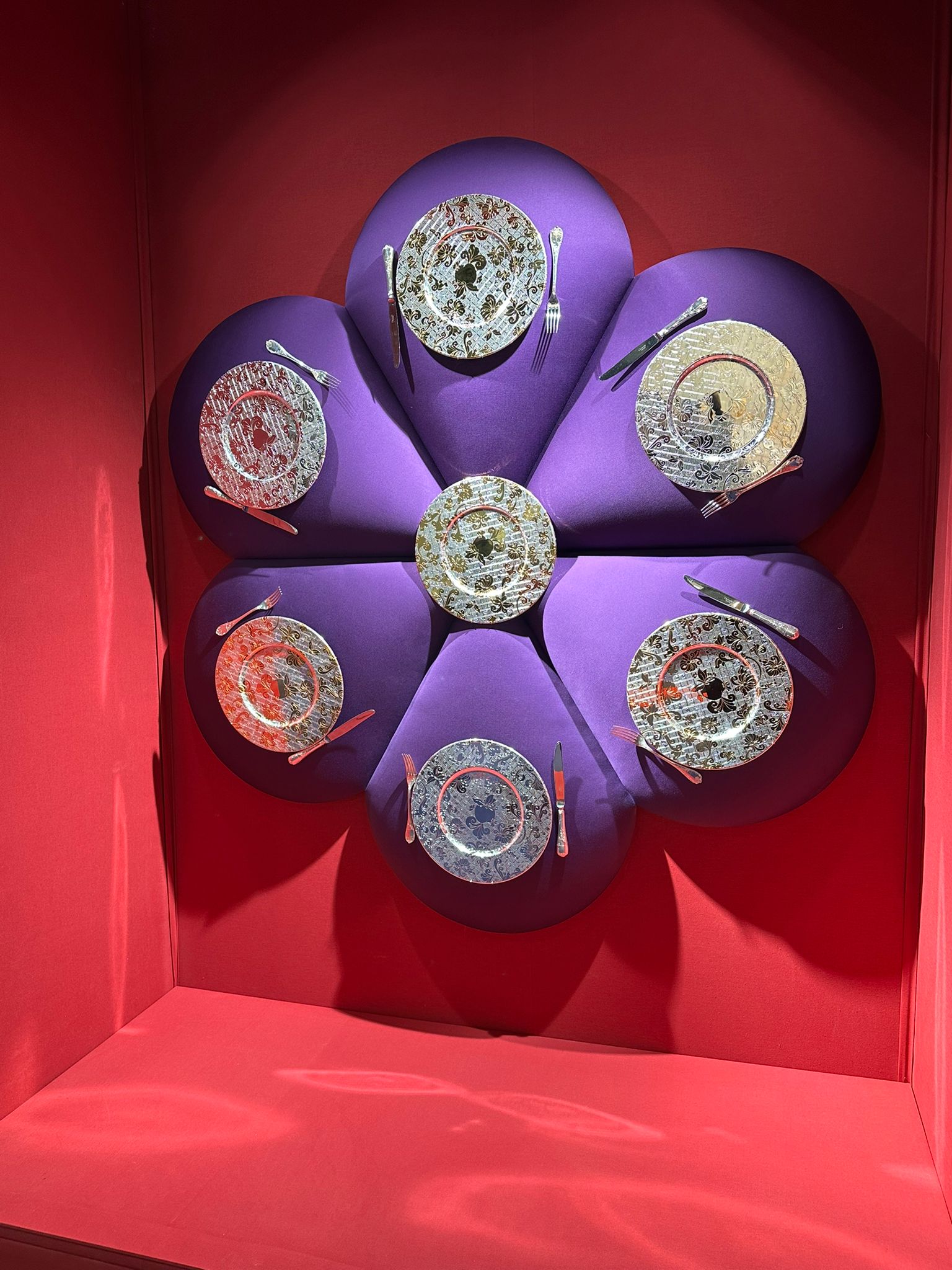 Künstlerisch arrangiertes Geschirr in floralem Design, präsentiert auf violettem Hintergrund in einer roten Box.