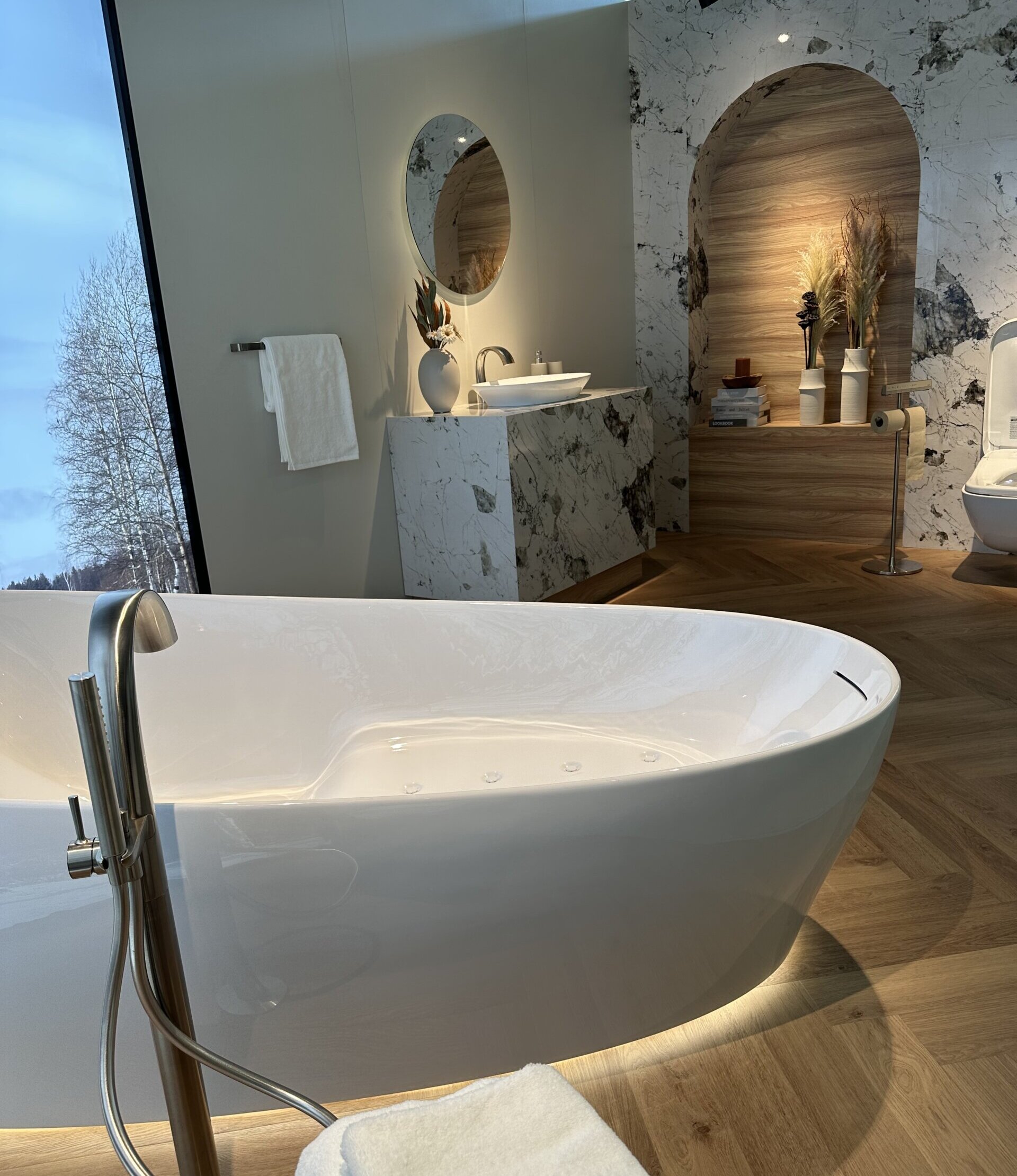 Freistehende Whirlpool-Badewanne in einem modernen Badezimmer mit Natursteinverkleidung, Holzfußboden und indirekter Beleuchtung für eine stilvolle Wellness-Atmosphäre.