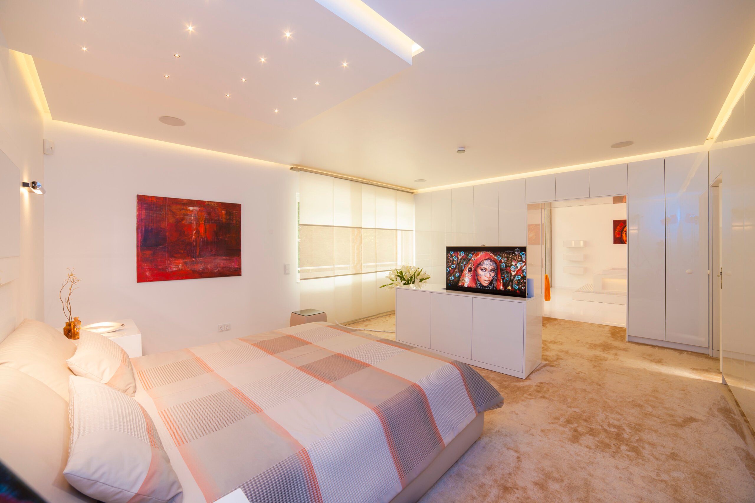 Modernes Schlafzimmer mit warmweißer Voutenbeleuchtung, TV-Lift und integriertem Badzugang