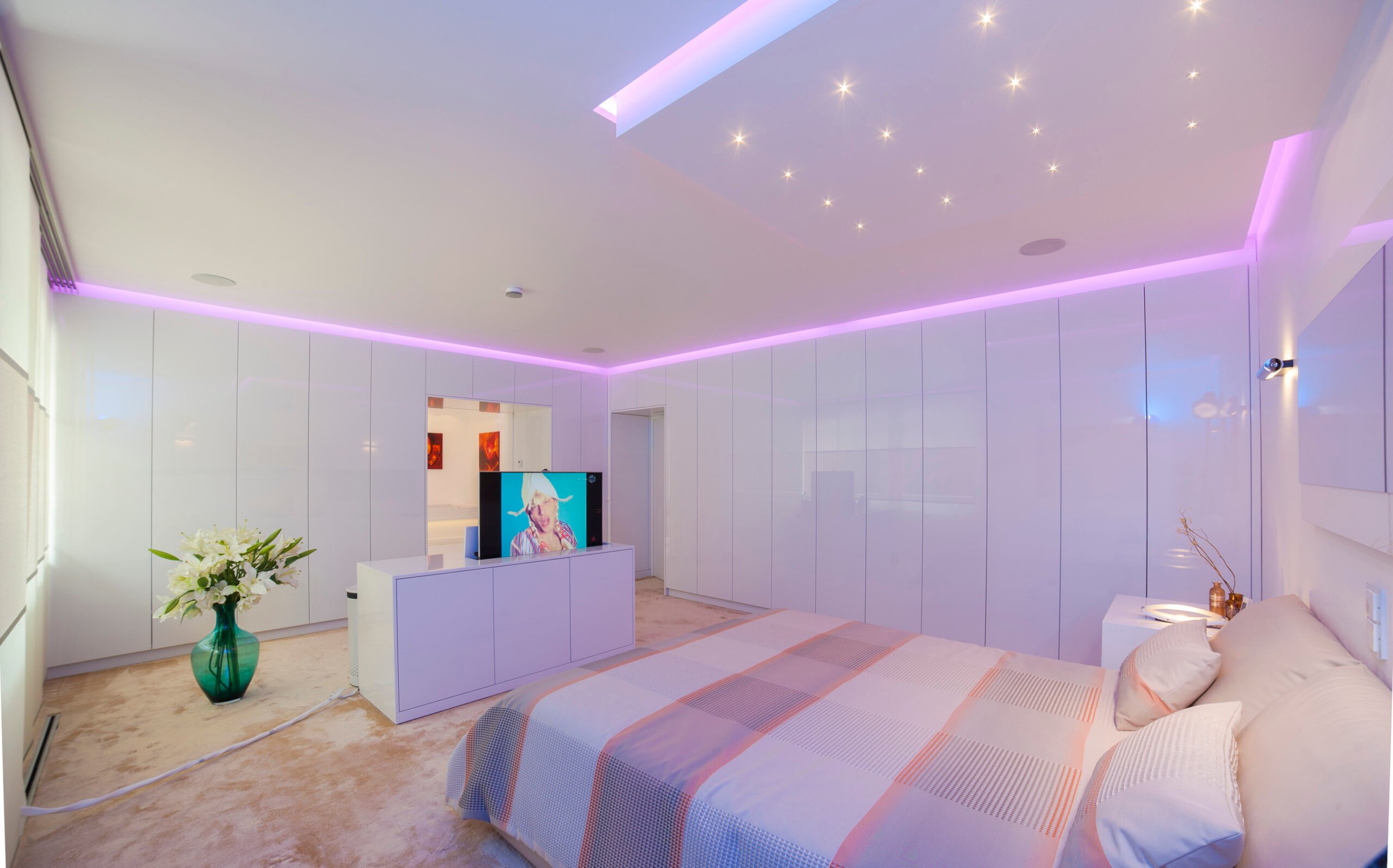 Modernes Schlafzimmer mit Sternenhimmel, roséfarbener Voutenbeleuchtung und vollintegriertem TV-Lift