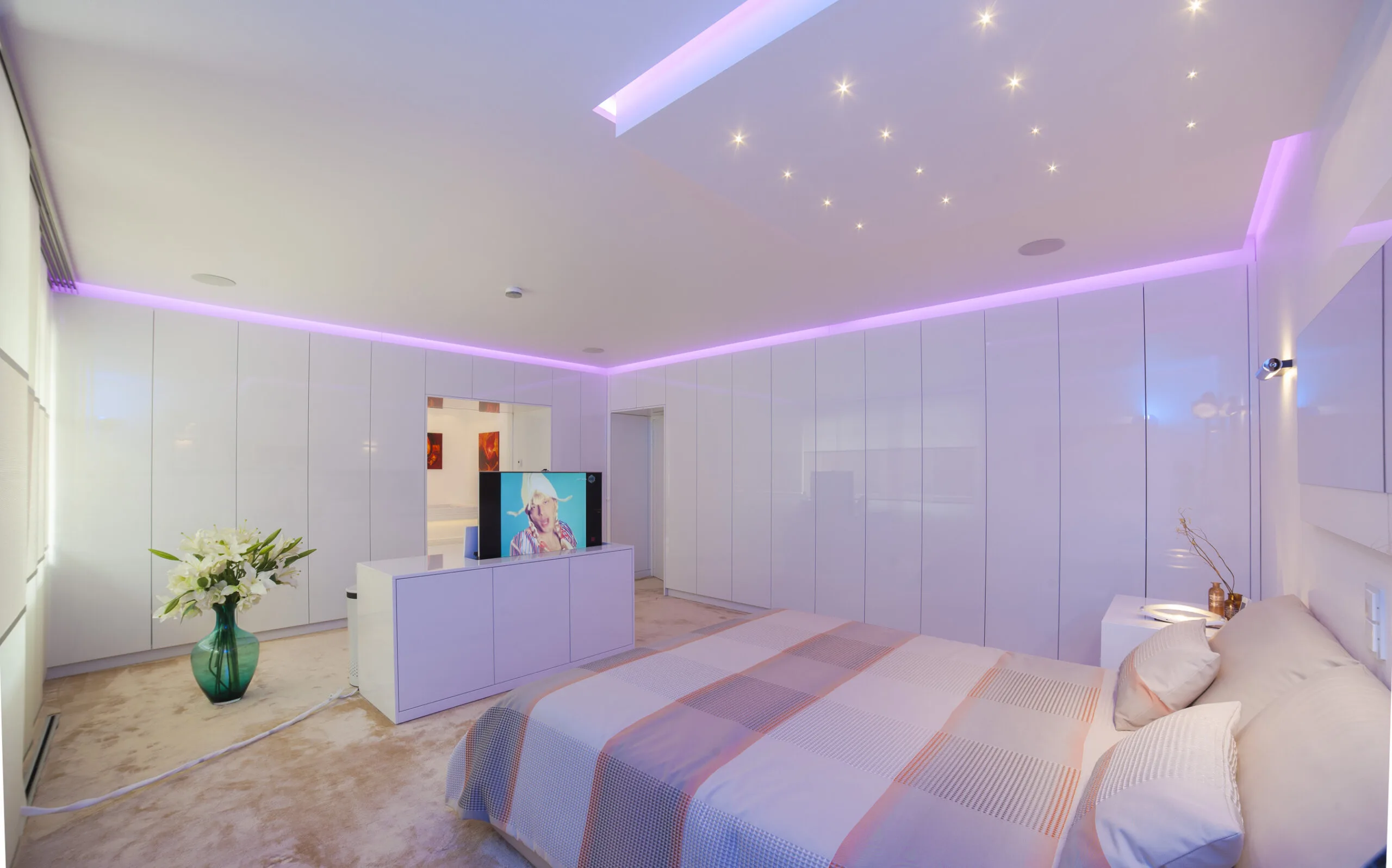 Modernes Schlafzimmer mit Sternenhimmel, roséfarbener Voutenbeleuchtung und vollintegriertem TV-Lift