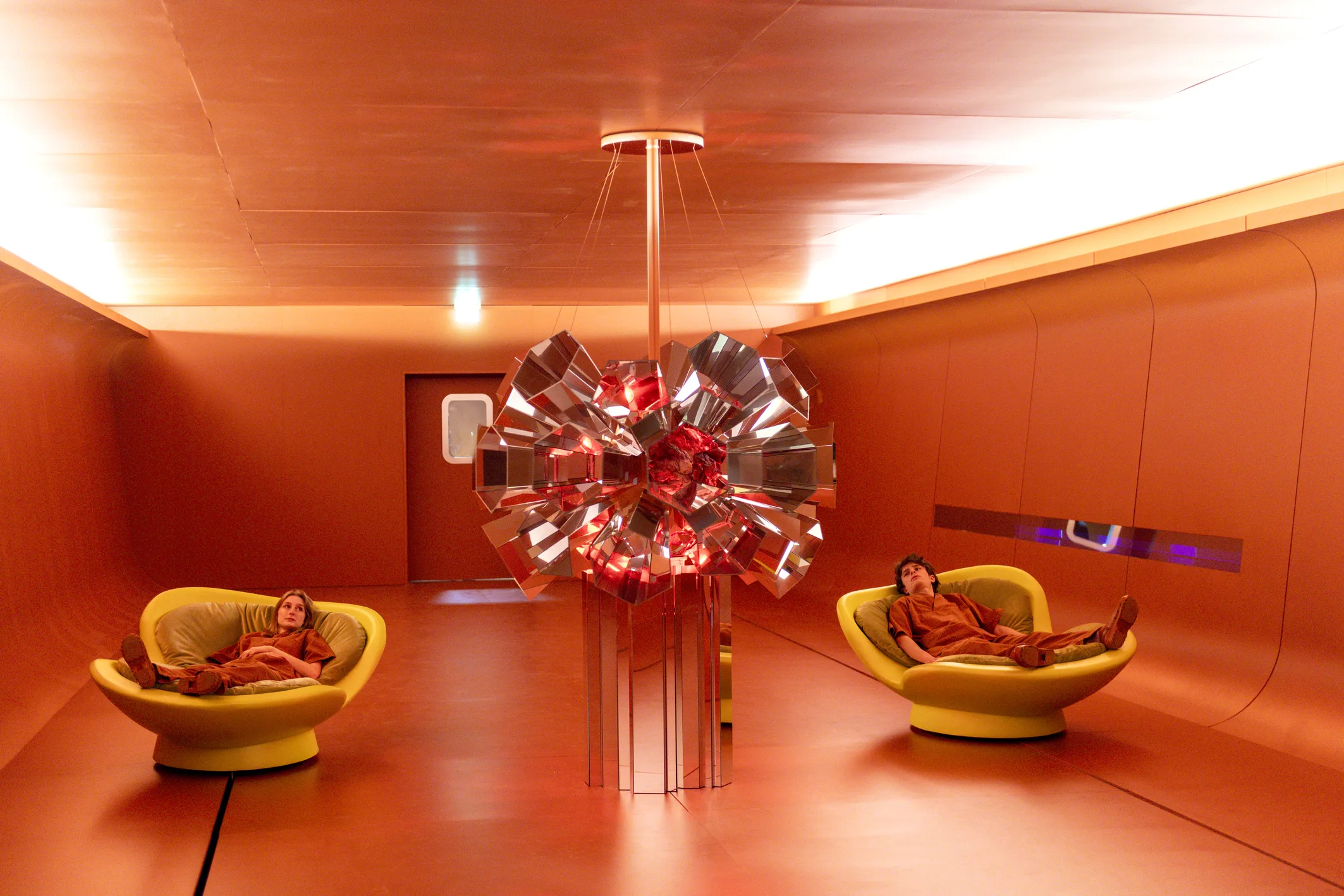 Zwei Personen entspannen in futuristischer, rot getauchter Rauminstallation mit zentralem Lichtobjekt auf dem Salone del Mobile 2025.