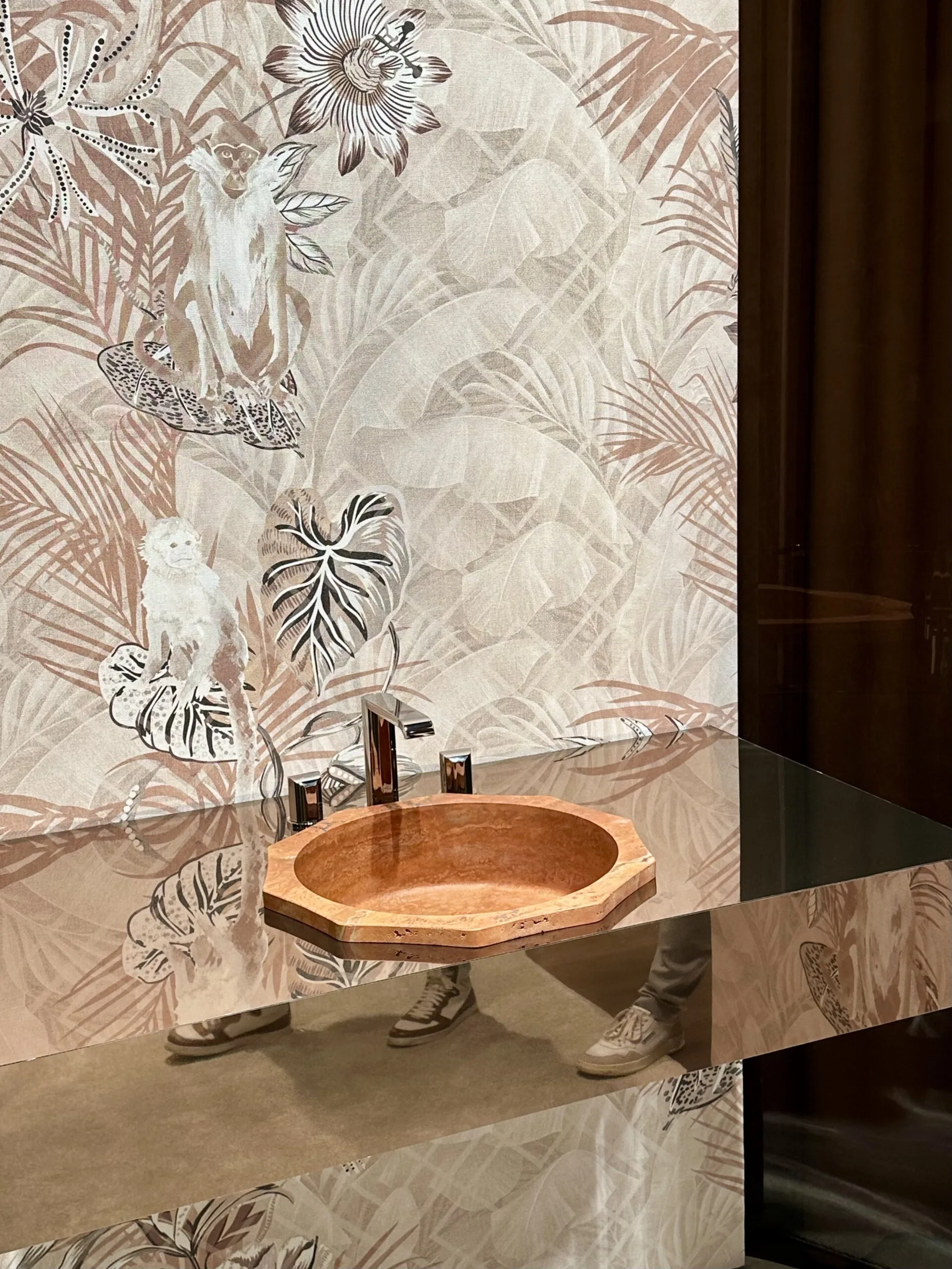 Waschtisch mit rotbrauner Naturstein-Schale vor floraler Designwand mit Tiermotiven.