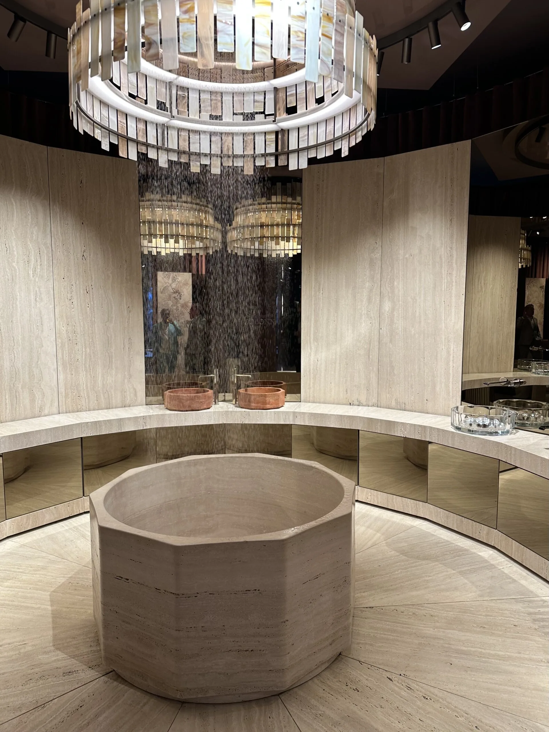 Casa Gessi Showroom Mailand – zentrales Natursteinbecken in Creme mit Regeninstallation und Lichtskulptur