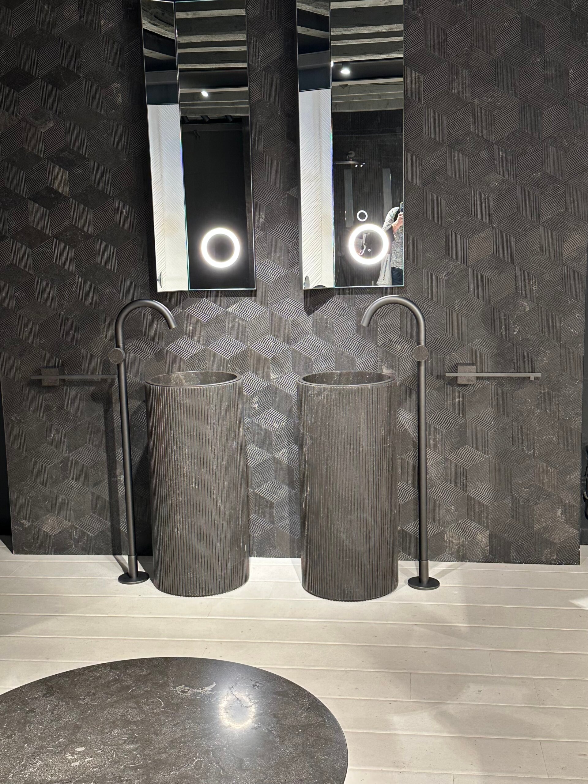 Doppelwaschtisch aus schwarzem Naturstein mit freistehenden Armaturen und geometrischer Wandgestaltung.