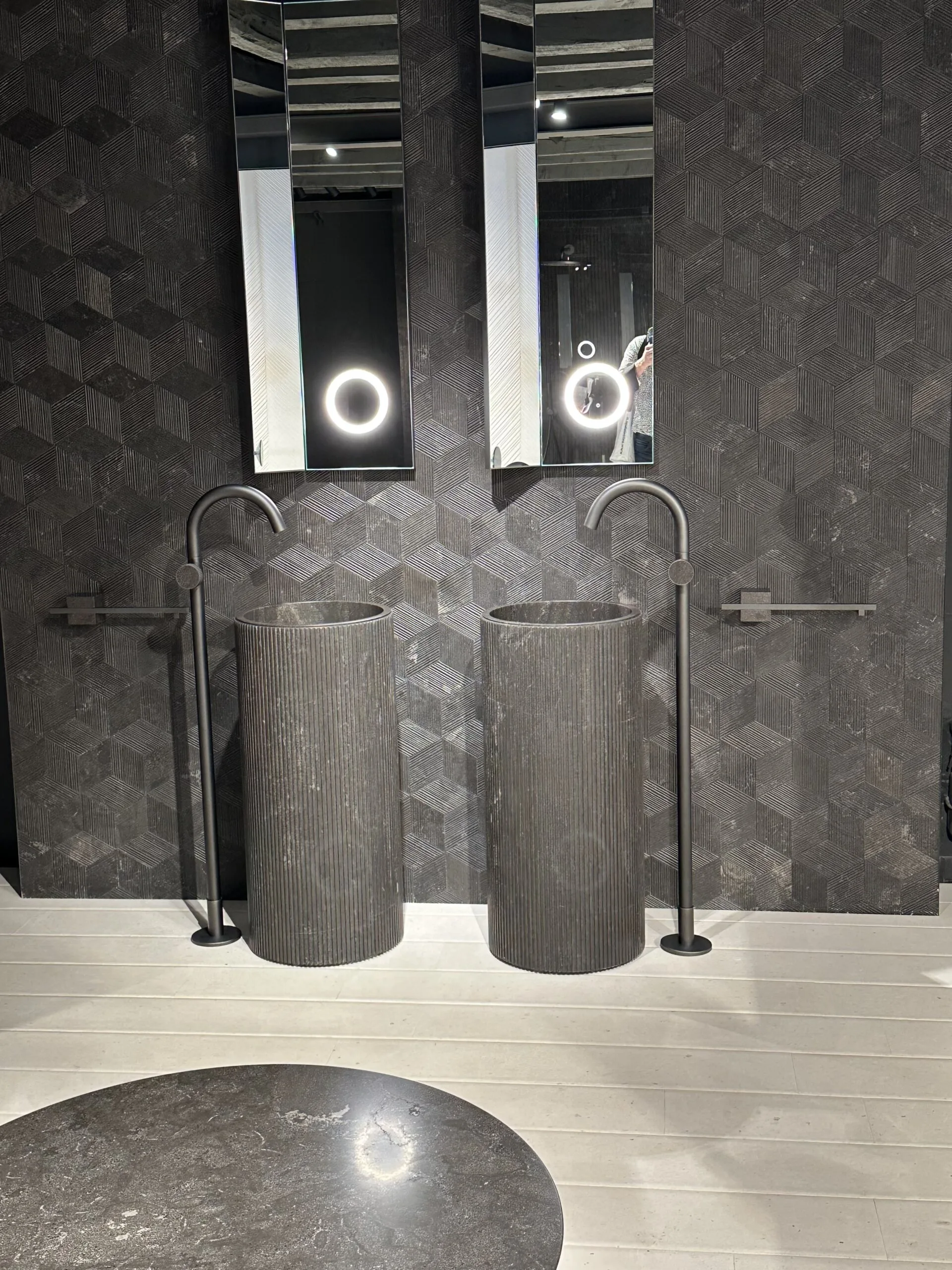 Doppelwaschtisch aus schwarzem Naturstein mit freistehenden Armaturen und geometrischer Wandgestaltung.