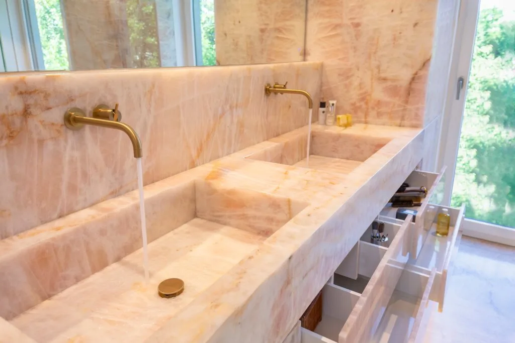 Doppelwaschtisch mit Armaturen von Vola in Gold. Bad und Private Spa mit rosa Naturstein, Design by Torsten Müller