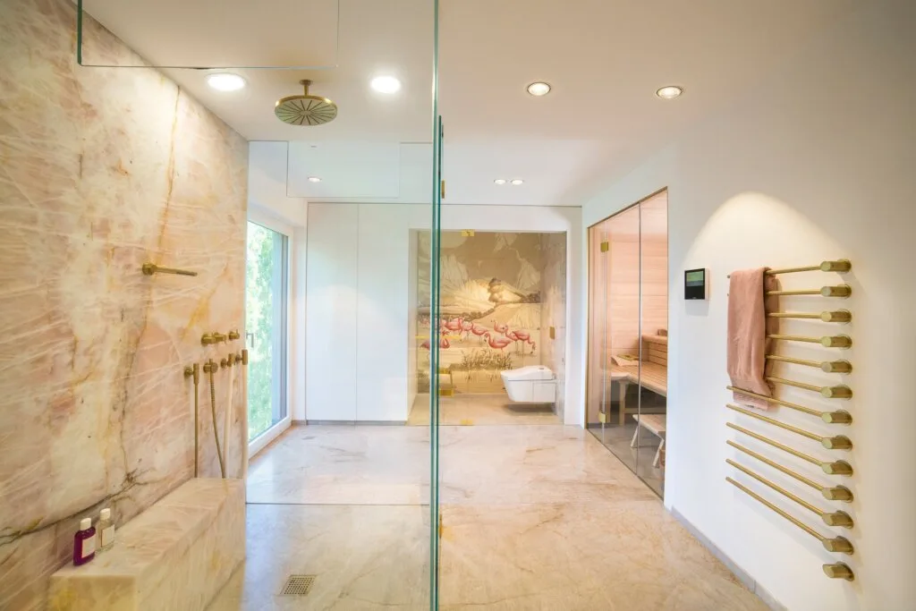 Blick durch die Kristalldusche in den WC-Raum. Bad und Private Spa mit rosa Naturstein, Design by Torsten Müller
