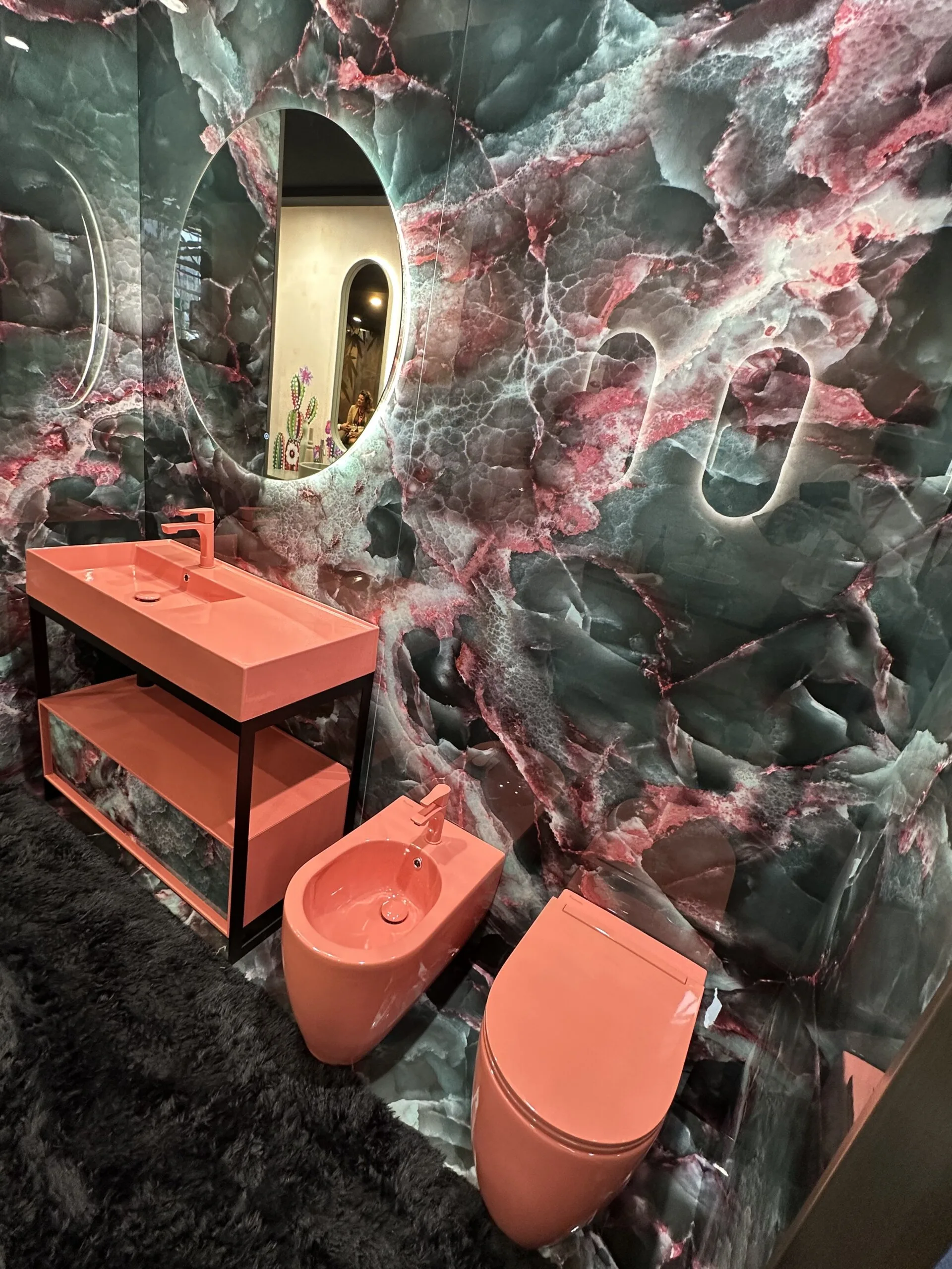 Modernes Badezimmer mit Tapete in Onyx-Optik und farbigen Sanitärobjekten in Korallenrot – kreatives Statement-Design.