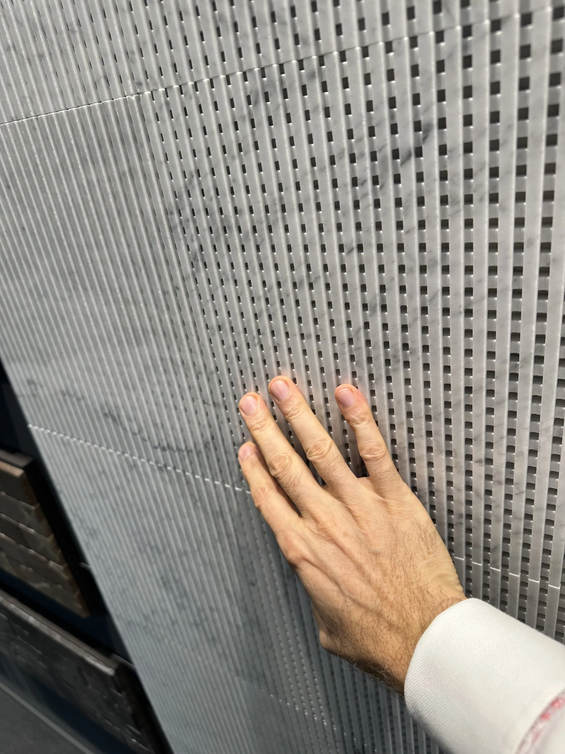 Eine Hand berührt eine graue Oberfläche mit eng gesetztem geometrischem Relief.