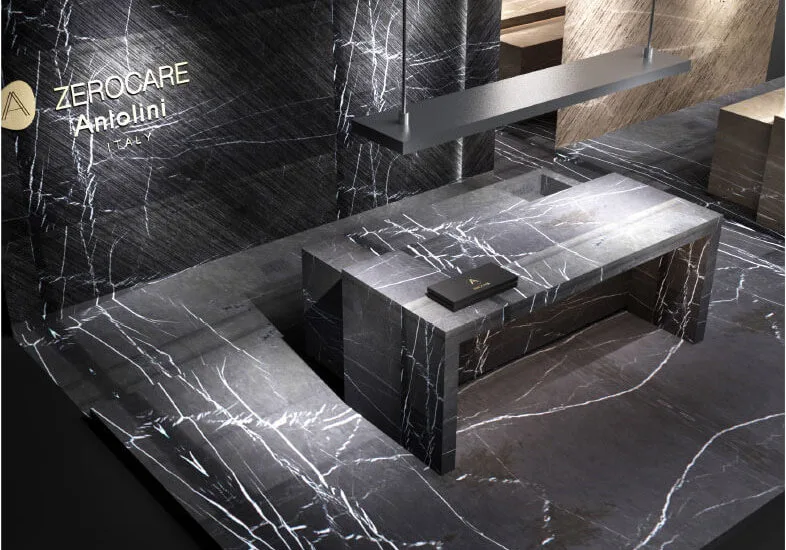 Verfeinerung und Innovation für Küchenräume mit imposanten skulpturalen Dimensionen Auf der IMM 2019 präsentiert Antolini ein beeindruckendes Display, das die Ausdrucksintensität von Naturstein steigert und sich gleichzeitig auf innovative Technologien konzentriert. Antolini, führend in der Herstellung von Naturstein und an der absoluten Spitze der Branche, nimmt an der IMM Cologne mit einer hoch entwickelten Installation des Designers Alessandro La Spada teil. Das harmonische und elegante Ausstellungsdisplay umfasst zwei Küchenblöcke, einer aus Bronze Amani und der andere aus Gray Stone: Wenn das erste Material mit seinen warmen, weichen, zarten Beige- und Cappuccino-Tönen fasziniert, die mit dunkleren Adern durchdrungen werden, überrascht das zweite Material durch seine flüchtige Persönlichkeit die verschiedene Grautöne mit schwer fassbaren weißen Adern abwechselt und ein abstraktes Design präsentiert, das so einzigartig ist, wie es nur die Natur bieten kann. Beide Küchenblöcke zeichnen sich durch eine lineare und geometrische Eleganz aus und verfügen über eine Schiebebrücke, die ihre Oberfläche verdoppelt und eine weitere verdeckte Oberfläche auf magische Weise enthüllt. Das Material von Amani Bronze und Grey Stone, das für die auf der IMM gezeigten Küchen verwendet wurde, wurde mit Azerocare behandelt. Azerocare wurde von Antolini patentiert und wurde speziell für Marmor, Onyx und weiche Quarzite entwickelt. Es handelt sich um eine revolutionäre Behandlung, die maximalen Schutz gegen Flecken und Ätzen durch Kontakt mit Nahrungsmitteln und sauren Substanzen garantiert. Azerocare wird von Antolini direkt auf die Plattenoberflächen aufgetragen und ist eine Garantie gegen mögliche Schäden, die durch die Verwendung von Produkten wie Wein, Kaffee, Öl, Essig, Tomatensauce und Fruchtsäften entstehen können, und ist daher die ideale Lösung für Oberflächen in Küchenumgebungen . Der elegante, graue Steinboden (Leder) vervollständigt das Gesamtbild und gibt der Installation ein Gefühl von Einheit. Über den Küchenblöcken ragen zwei lange Deckenleuchten mit Bronze- und gebürstetem Stahlüberzug hervor. Dahinter und auf einer Seite befinden sich die majestätischen und markanten Wände aus Gray Stone I Stratos Design und Bronze Amani I Stratos Design, die zart von geräucherten Spiegeln unterbrochen werden, die die Pracht des Steins mit überraschendem Stil widerspiegeln.