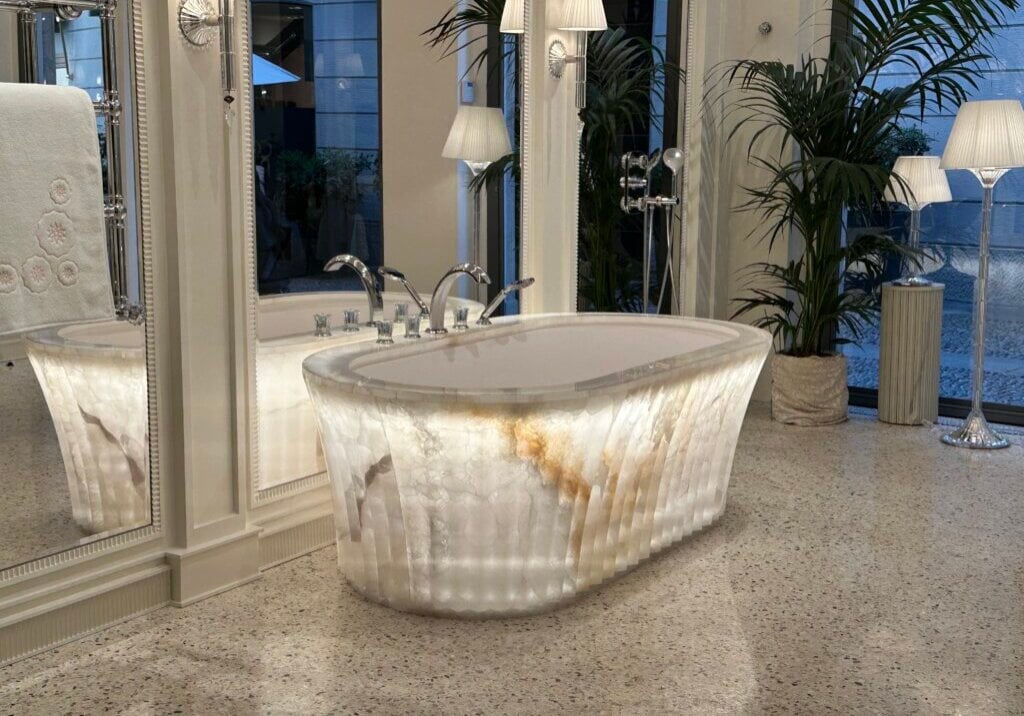 Beleuchtete freistehende Luxus-Badewanne aus Onyx in einem eleganten Spa-Badezimmer mit Spiegelflächen und Palmen.