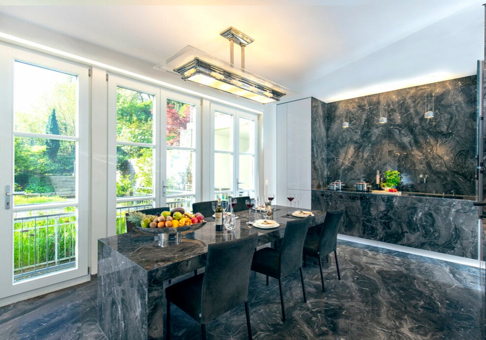 Blick in den Garten über den luxuriösen Naturstein-Tisch mit Einblick in die Küchenzeile