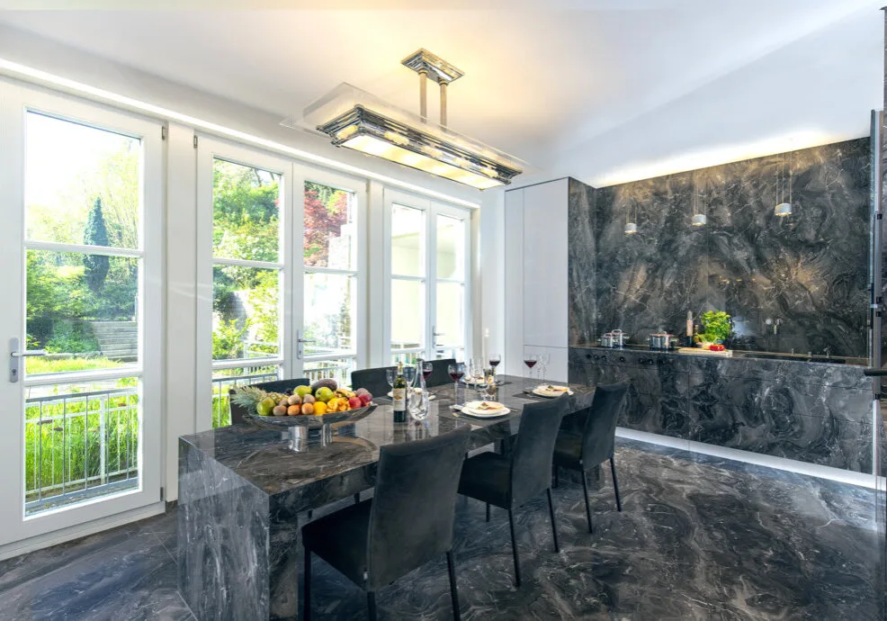 Blick in den Garten über den luxuriösen Naturstein-Tisch mit Einblick in die Küchenzeile