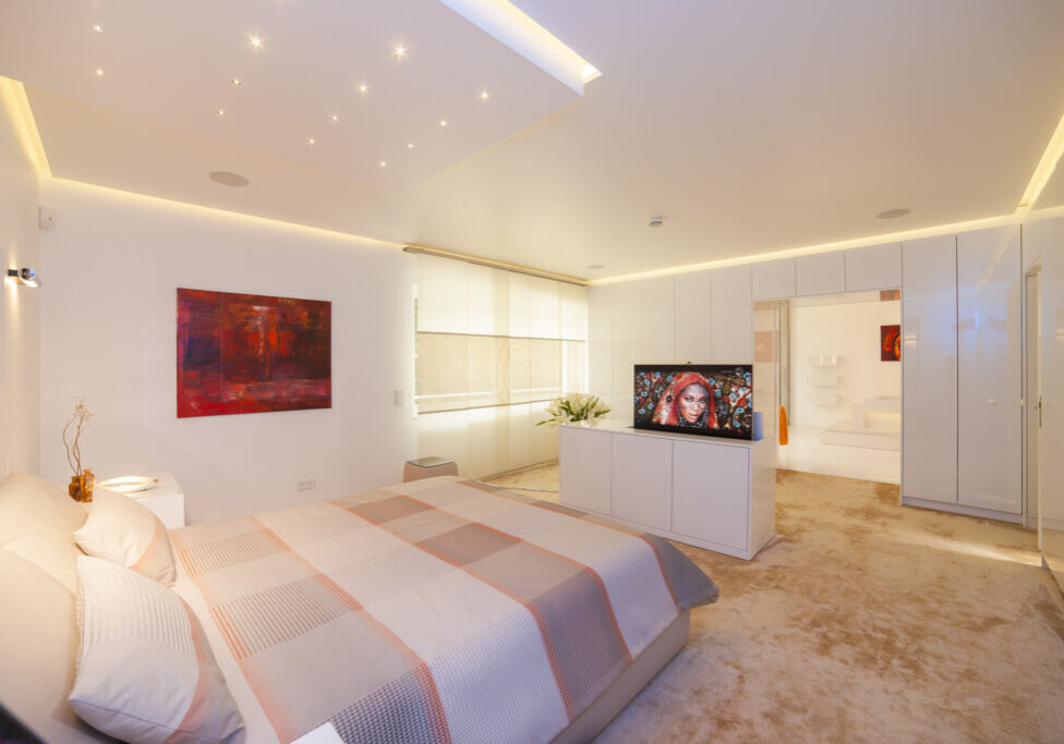 Modernes Schlafzimmer mit warmweißer Voutenbeleuchtung, TV-Lift und integriertem Badzugang
