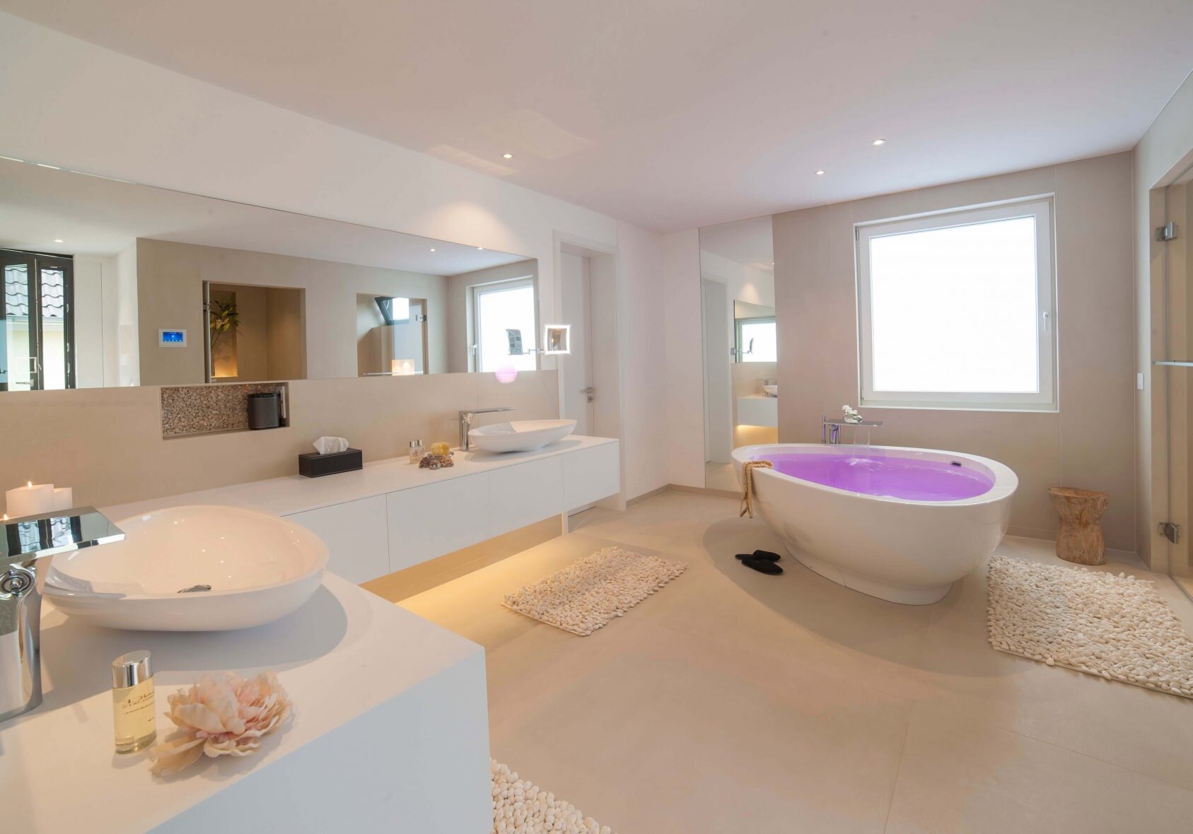 Wellness bad zu Hause Badezimmer Wellnessbereich Luxus Traumbad Design by Torsten Mueller Cologne (4) Wellnessbad im eigenen Zuhause Sich in den eigenen vier Wänden der wohltuenden Atmosphäre eines Spa hinzugeben, ist der Traum vieler Hausherren. In diesem Fall hat Design by Torsten Müller aus Bad Honnef nähe Köln / Bonn diesen Traum verwirklicht und ein echtes Wellness-Paradies geschaffen. In dem abgetrennten Duschbereich findet sich das BIG RAIN Regenpanel WATER MODULES von Dornbracht, das einen anregenden Schauer oder einen sanften Tropenregen genauso inszenieren kann, wie auch einen erfrischenden Sommerregen. Das Lichtdesign ist der Smart Home Installation zu verdanken, die individuelle Szenarien wahr werden lassen und kaum Wünsche offenlassen. Die fugenlose Waschtisch-Konstruktion ist aus dem Werkstoff Corian gefertigt und nach einem individuellen Maß hergestellt. Die freistehende Badewanne vom Designer Jean-Marie Massaud, in der lange Stunden voller Müßiggang möglich sind, stammt von AXOR. Lassen Sie sich inspirieren und wagen Sie es, Ihren ganz persönlichen Wohlfühlraum von einer Wellness-Oase im eigenen Haus gemeinsam mit Design by Torsten Müller wahr werden zu lassen.