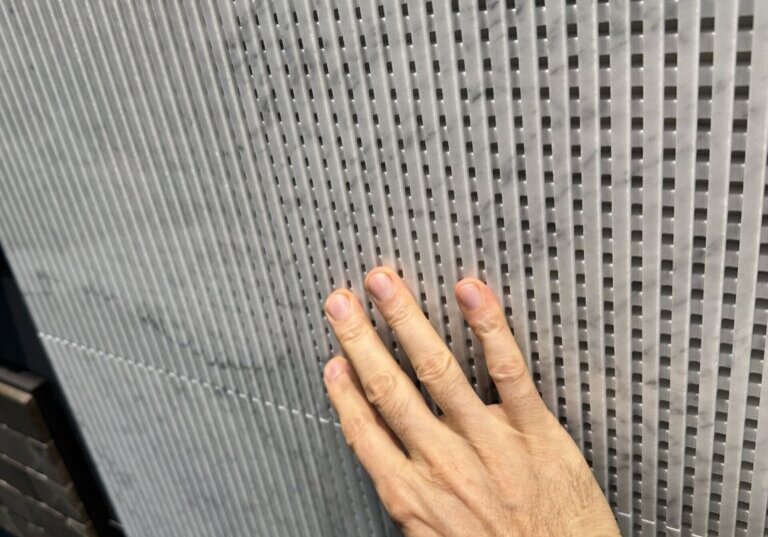 Eine Hand berührt eine graue Oberfläche mit eng gesetztem geometrischem Relief.