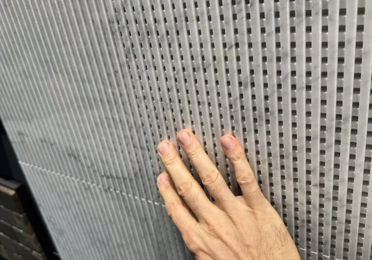 Eine Hand berührt eine graue Oberfläche mit eng gesetztem geometrischem Relief.