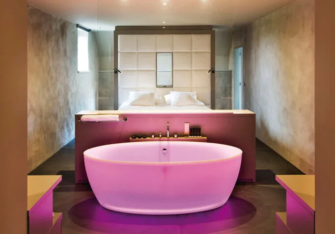 Doppelbett mit smarter Badewanne davor in violettem Licht